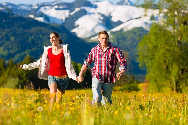 Casal correndo no prado com montanha — Fotografia de Stock