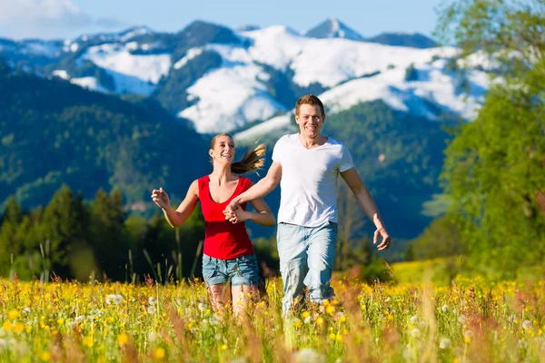 Pareja corriendo en el prado con montaña —  Fotos de Stock