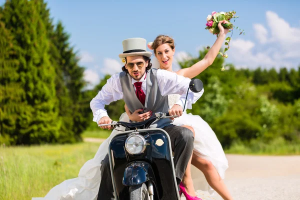 Pareja nupcial que conduce la vespa del motor que usa vestido y traje — Foto de Stock