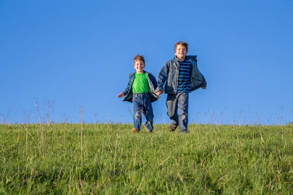 Två pojkar kör tillsammans på grön kulle — Stockfoto