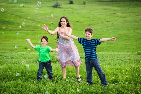 Drie kinderen vangen de zeepbellen op gazon — Stockfoto