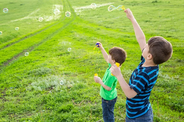 Two boys blowing up the soap bubbles on lawn — Stock Photo, Image