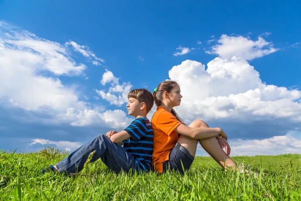 Zwei Kinder, die Rücken an Rücken im Gras sitzen — Stockfoto