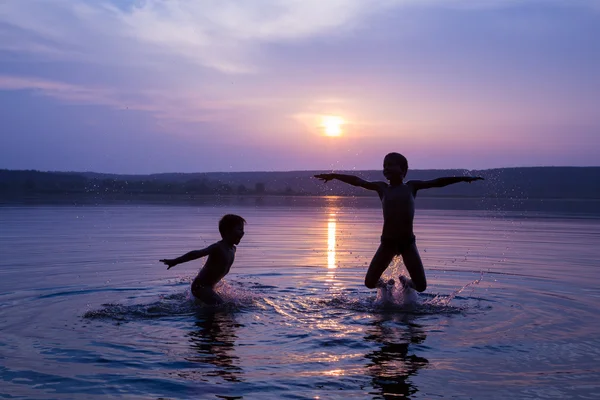 Two boys jumping into water on sunset — Stock Photo, Image