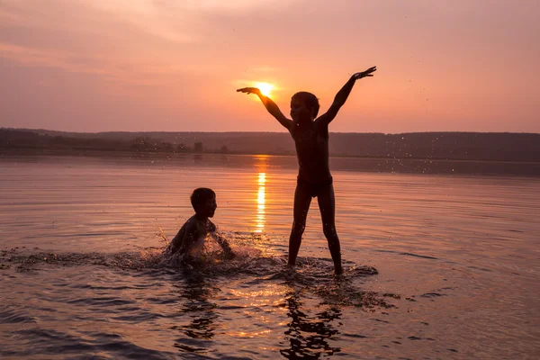 Two boys jumping into water on sunset — Stock Photo, Image