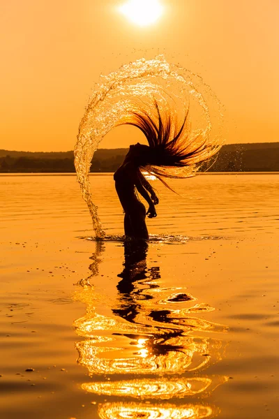 Silhouette di giovane ragazza in acqua spruzzando i capelli — Foto Stock