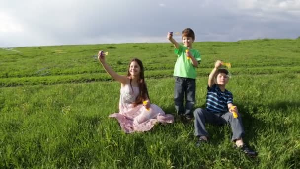 Tre bambini che fanno esplodere le bolle di sapone sulla collina — Video Stock