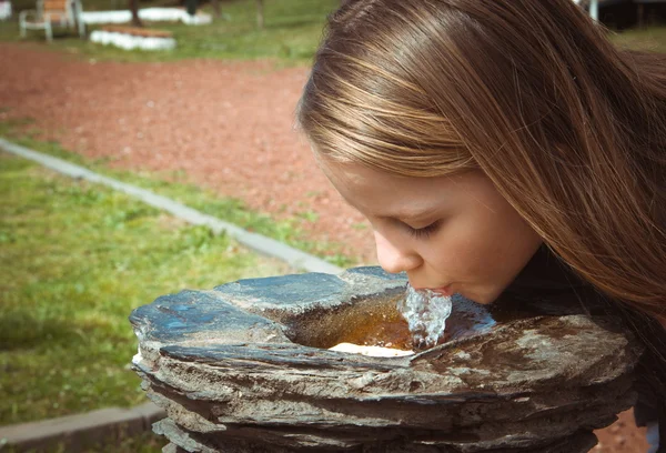 little girl drinking from water fountain in park