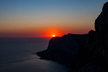 Körfez kıyısının silueti, yukarıdan gökyüzü açık kırmızı günbatımı manzaralı.