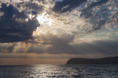 Güneş denizin üzerindeki bulutların arasından aydınlanıyor. Sahil gün batımı