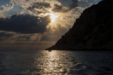 Güneş denizin üzerindeki bulutların arasından aydınlanıyor. Sahil gün batımı