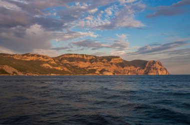Güneş denizin üzerindeki bulutların arasından aydınlanıyor. Sahil gün batımı