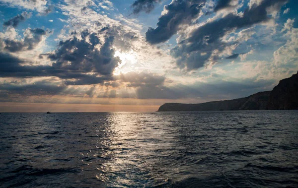 Güneş denizin üzerindeki bulutların arasından aydınlanıyor. Sahil gün batımı
