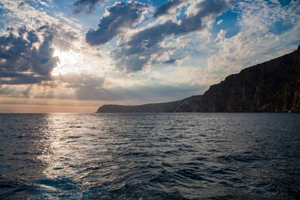 Güneş denizin üzerindeki bulutların arasından aydınlanıyor. Sahil gün batımı