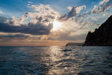 Güneş, denizin üzerindeki bulutların arasından aydınlanıyor.