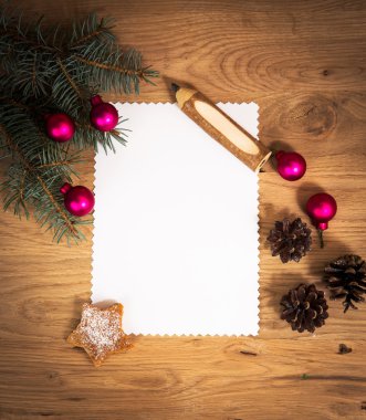 Ahşap zeminde boş bir kağıt tabaka. Kalem ve Noel süslemeleri ile birlikte.