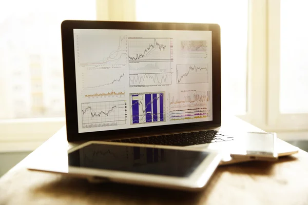 Énzügyi grafikon a képernyőn a laptop és tabletta munkahely — Stock Fotó