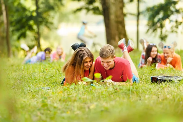 Par framgångsrika studenter med en lärobok i en park på en solig dag — Stockfoto