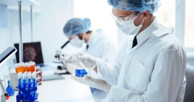 Kapat. Bir bilim adamının ellerinde bir şişe mavi sıvı..