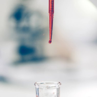 Kapat. Laboratuvar pipetinde bir damla kırmızı sıvının arkaplan resmi.