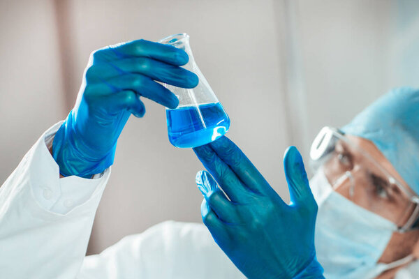 учёный в защитной одежде смотрит на жидкость во фляжке.