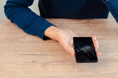 Mutsuz genç bir adam kırık bir ekranla akıllı telefonuna bakıyor..