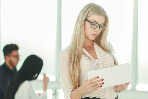 Femme d'affaires sérieuse avec tablette numérique debout près du bureau — Photo