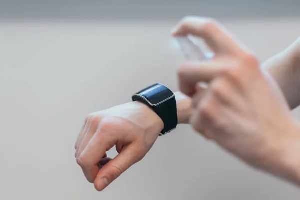 Casual man spraying alcohol antiseptic on his smart watch. — Stock Photo, Image