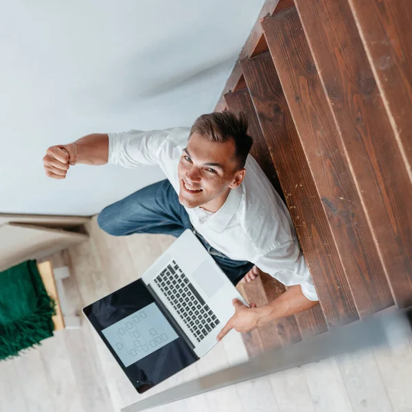 Ung man med en bärbar dator sitter på trappan i sin lägenhet. — Stockfoto