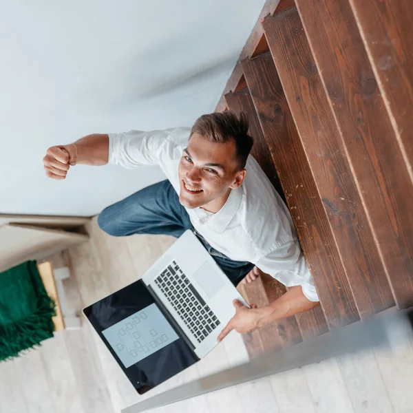 Junger Mann mit Laptop sitzt auf den Stufen in seiner Wohnung. — Stockfoto