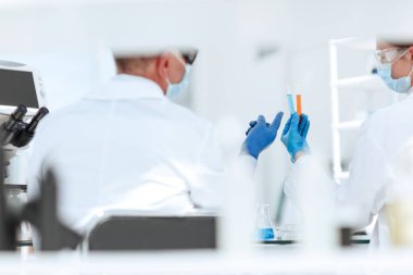 Dikiz aynası. Mikrobiyoloji bilimcileri test tüplerindeki sıvıyı tartışıyor..