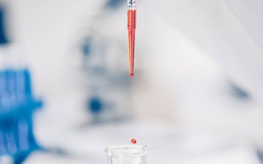 Bulanık bir arkaplanda laboratuvar pipetinde kırmızı sıvı.