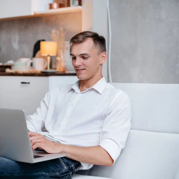 Jovem está trabalhando em um laptop enquanto sentado no sofá. — Fotografia de Stock