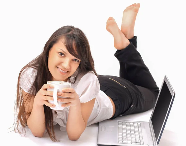 Atractiva joven con una taza de café tumbado frente a un ordenador portátil abierto. — Foto de Stock