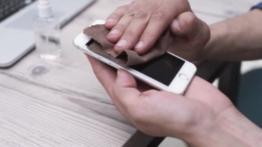 Adam akıllı telefonunu bakteriyel bir bezle dikkatlice dezenfekte ediyor. Kapat - kapat
