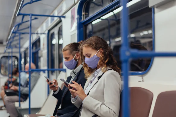 Passageiros usando máscaras protetoras usando seus smartphones enquanto sentados em um carro de metrô. — Fotografia de Stock