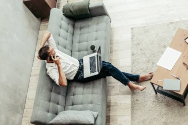 Genç adam akıllı bir telefonla konuşuyor, kanepede oturuyor..