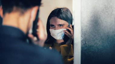 Kapat. Koruyucu maskeli üzgün genç çift birbirlerine bakıyorlar..