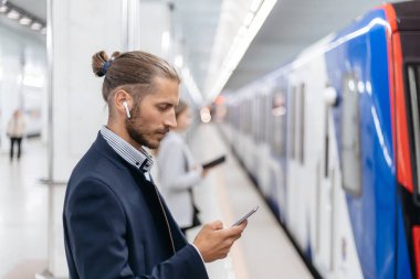 Genç adam metro istasyonunda dururken SMS okuyor..