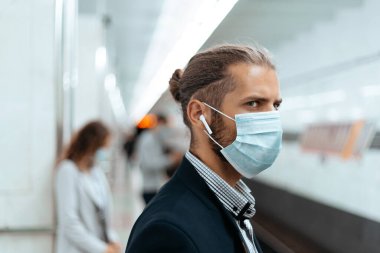 Metro istasyonunda duran koruyucu maskeli genç adam..