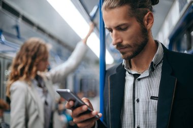 Genç adam akıllı telefonunu metroda kullanıyor..