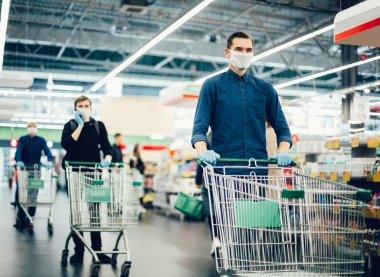 Elinde alışveriş arabası olan koruyucu maskeli genç bir adam.