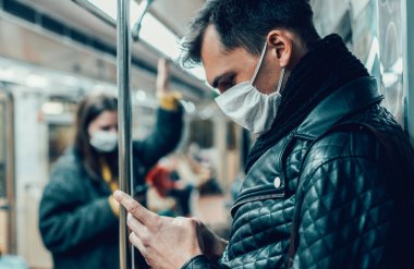 Koruyucu maskeli yolcu akıllı telefonundan bir mesaj okuyor..