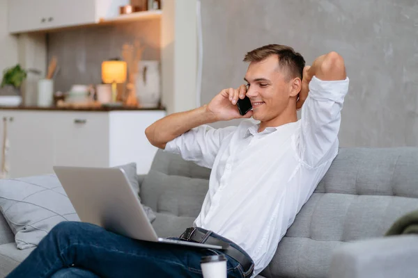 Ung man med en bärbar dator talar på en smartphone. — Stockfoto