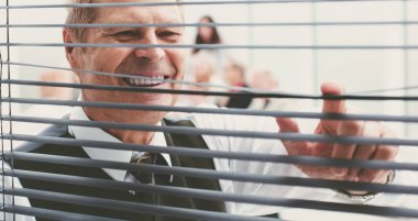 Kapat. Neşeli ofis çalışanı pencere perdelerinden bakıyor..