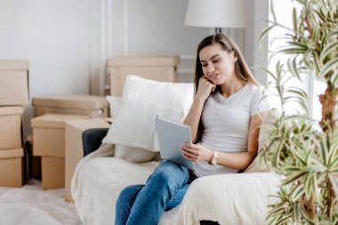 Dijital tabletli genç bir kadın rahat bir koltukta oturuyor.