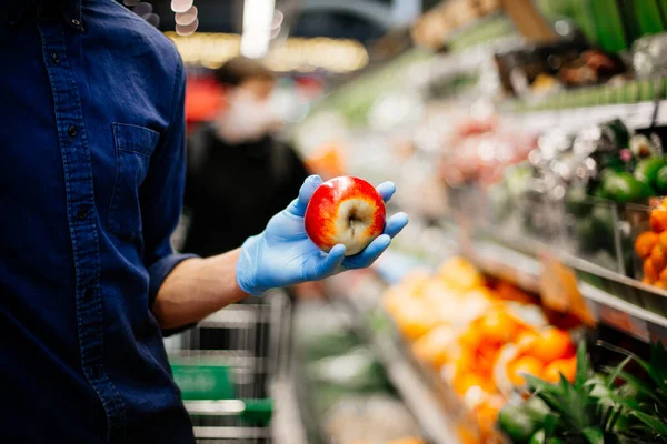 Man in a protective mask when selecting apples at the supermarket. — Stock Photo, Image