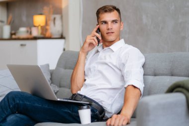 Genç adam akıllı bir telefonla konuşuyor, kanepede oturuyor..