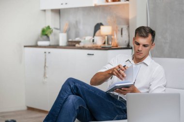 Genç adam kanepede oturmuş notlar alıyor. .