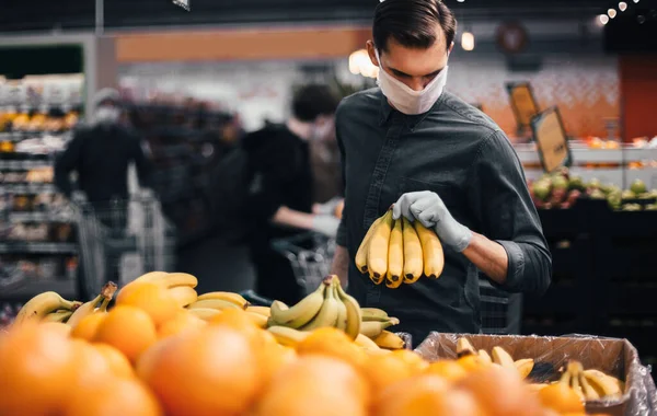 Homme en gants de protection choisir des bananes dans un supermarché. — Photo
